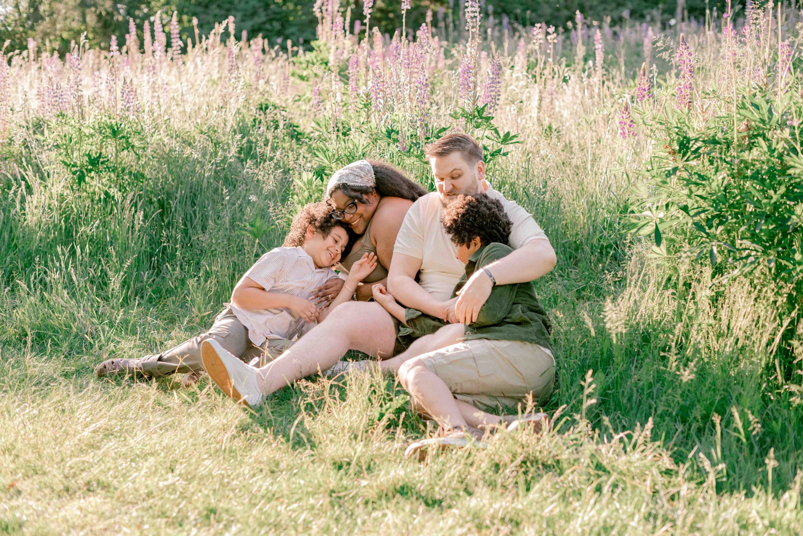 family of four sit and play in the lupine field in family photoshoot at Discovery Park