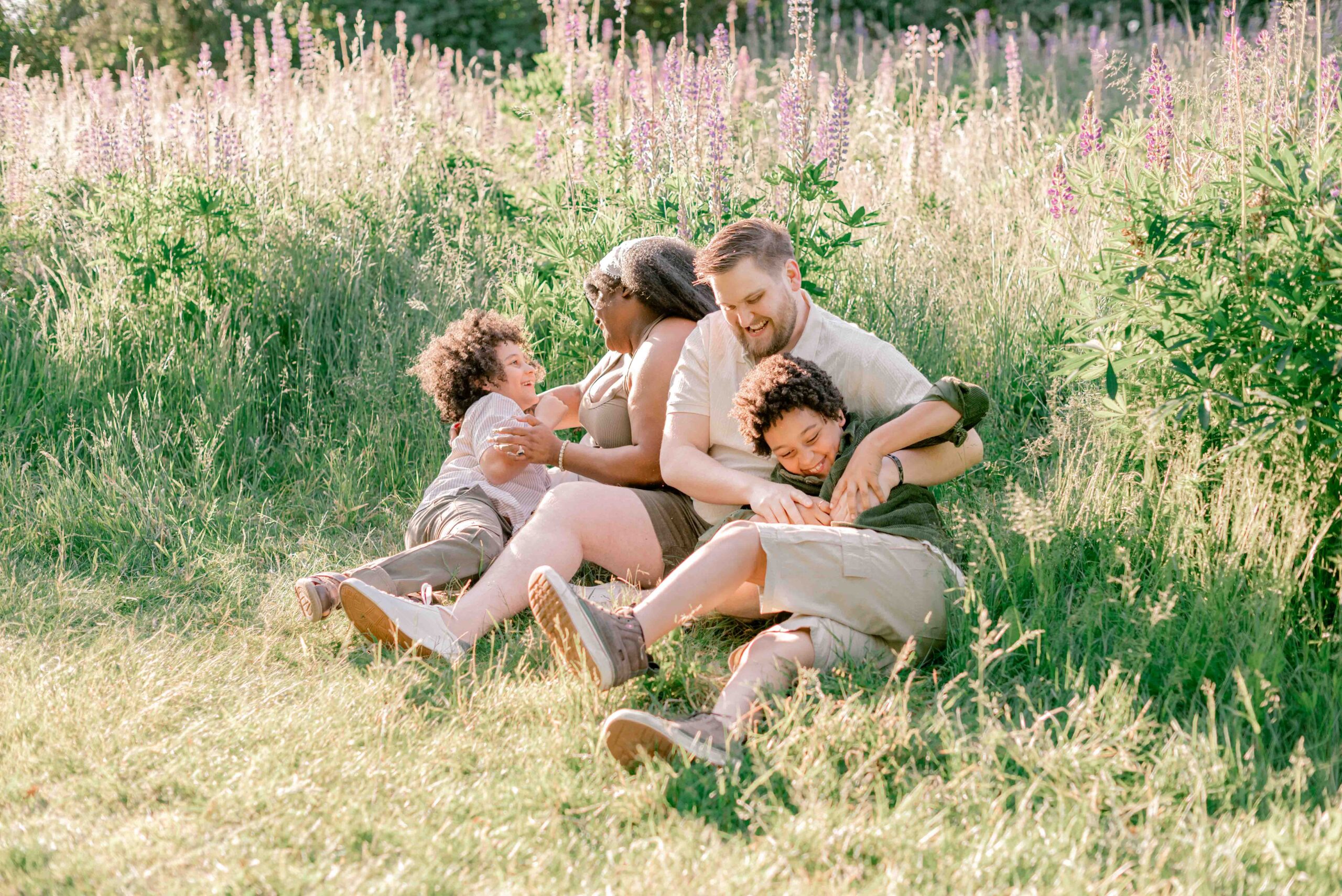 family of four sit and play in the lupine field in family photoshoot at Discovery Park