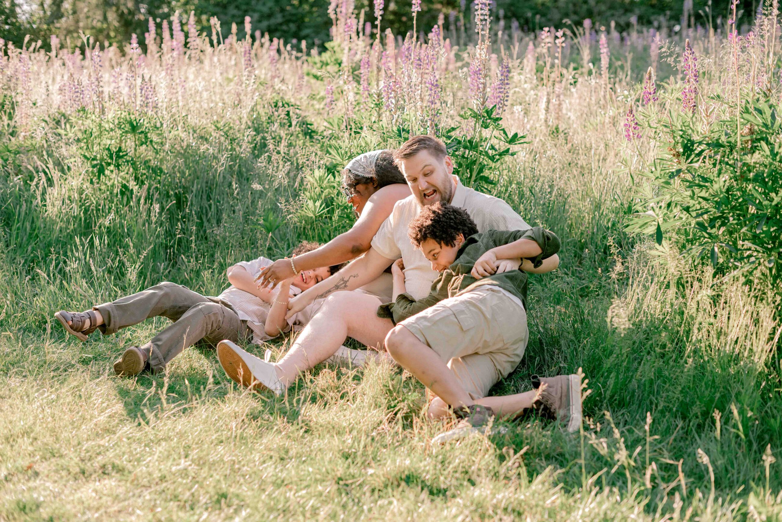 family of four sit and play in the lupine field in family photoshoot at Discovery Park