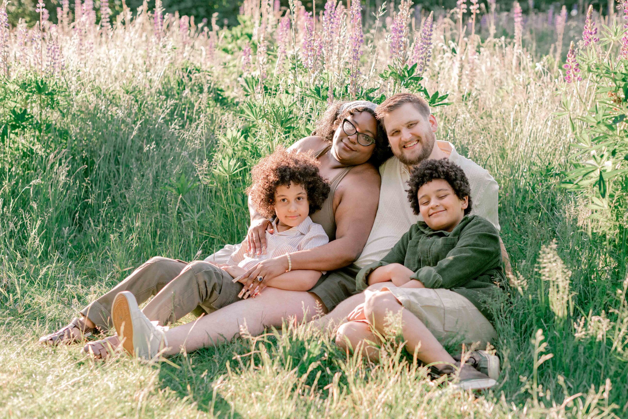 family of four sit in the lupine field in family photoshoot at Discovery Park