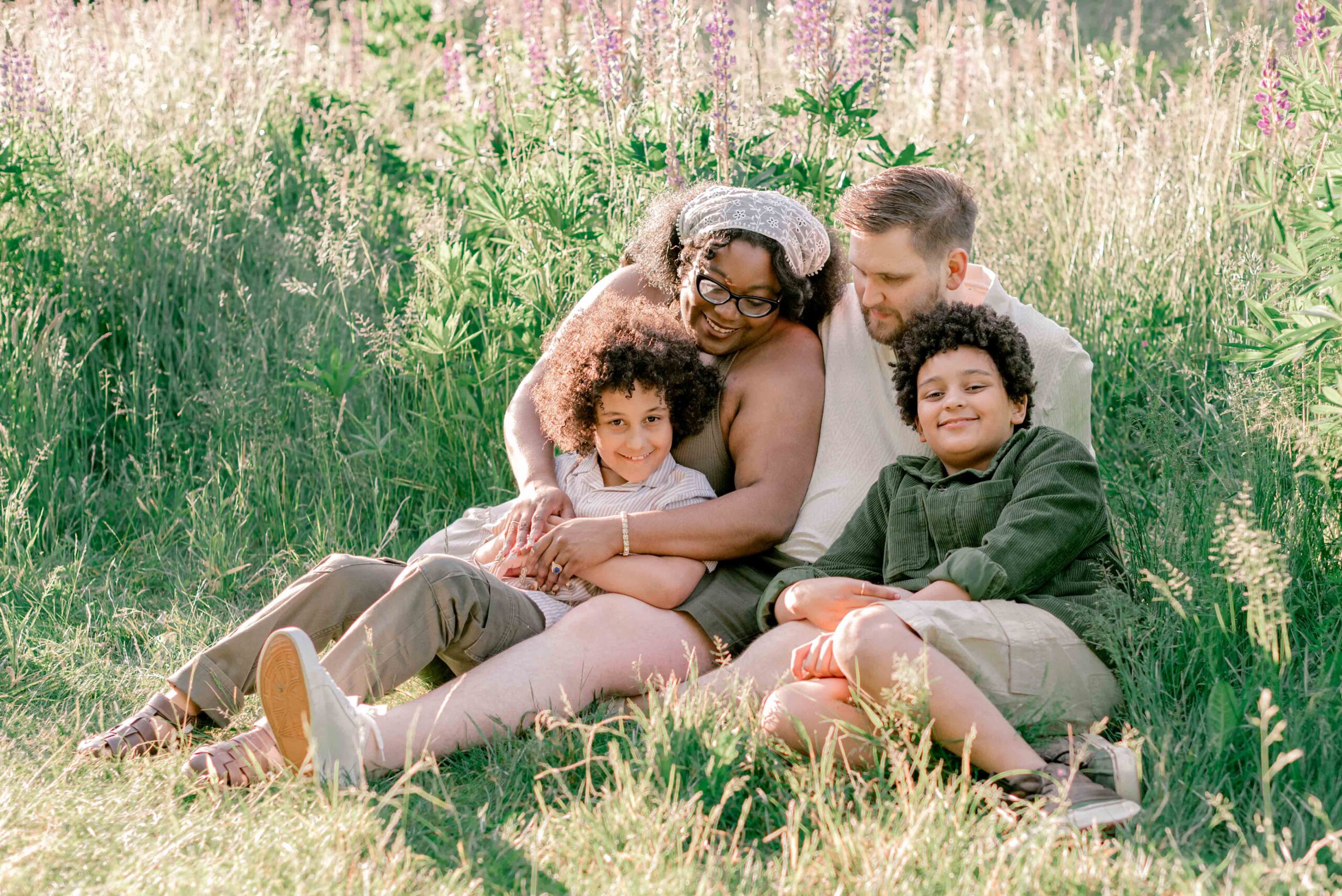 family of four sit in the lupine field in family photoshoot at Discovery Park