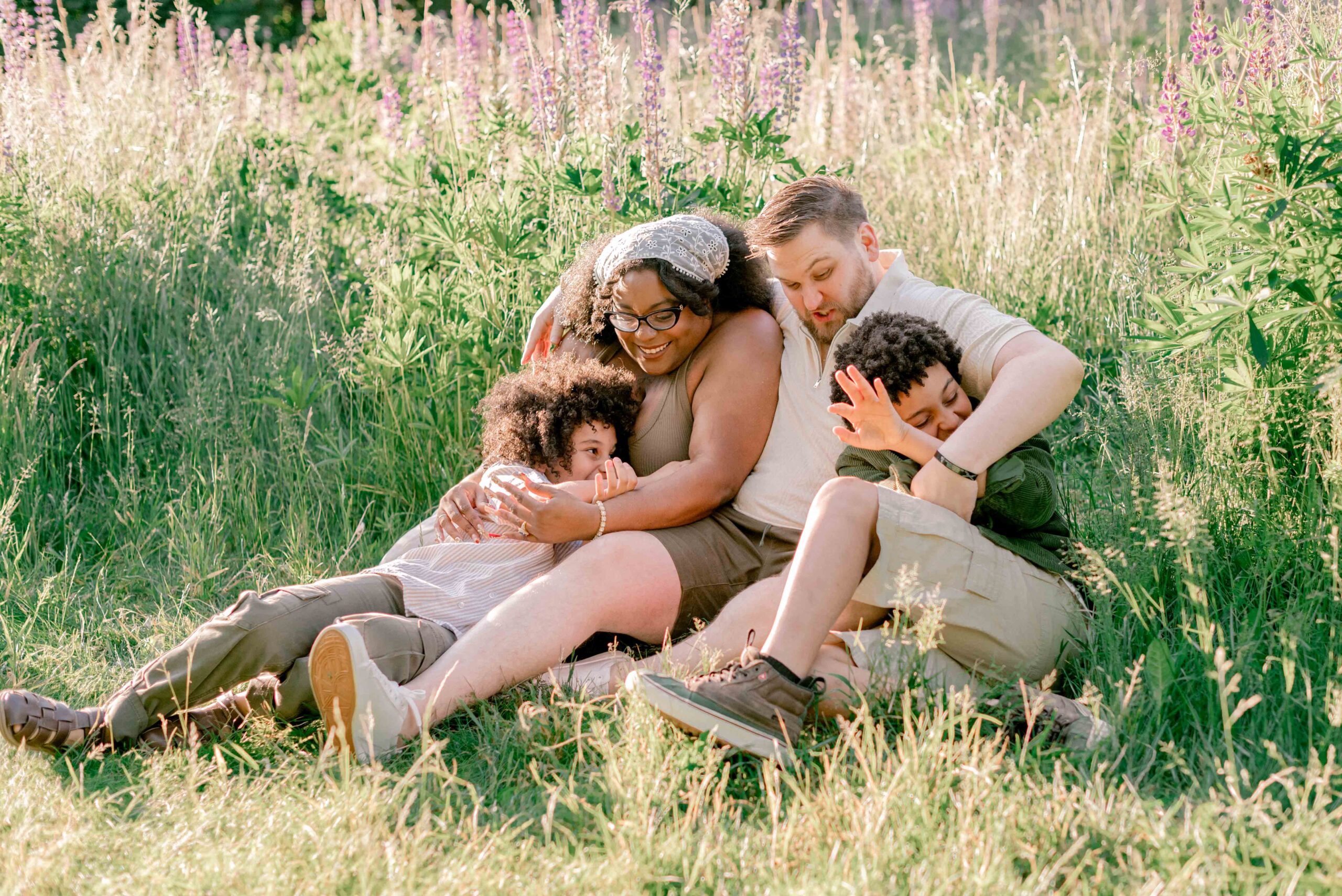 family of four sit and play in the lupine field in family photoshoot at Discovery Park