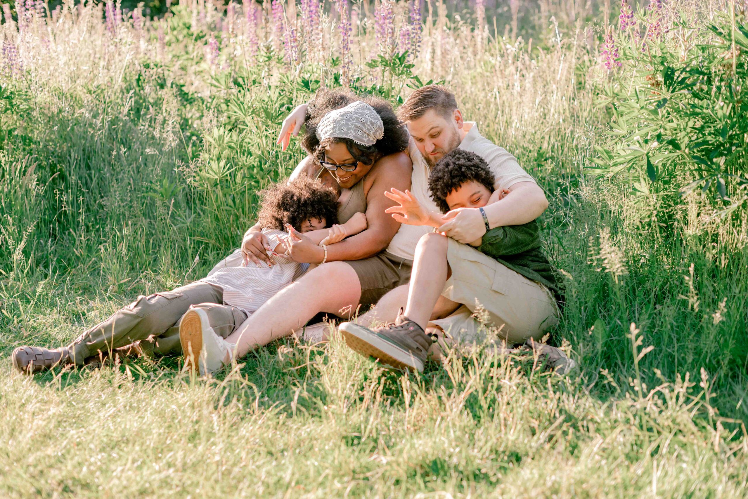 family of four sit and play in the lupine field in family photoshoot at Discovery Park