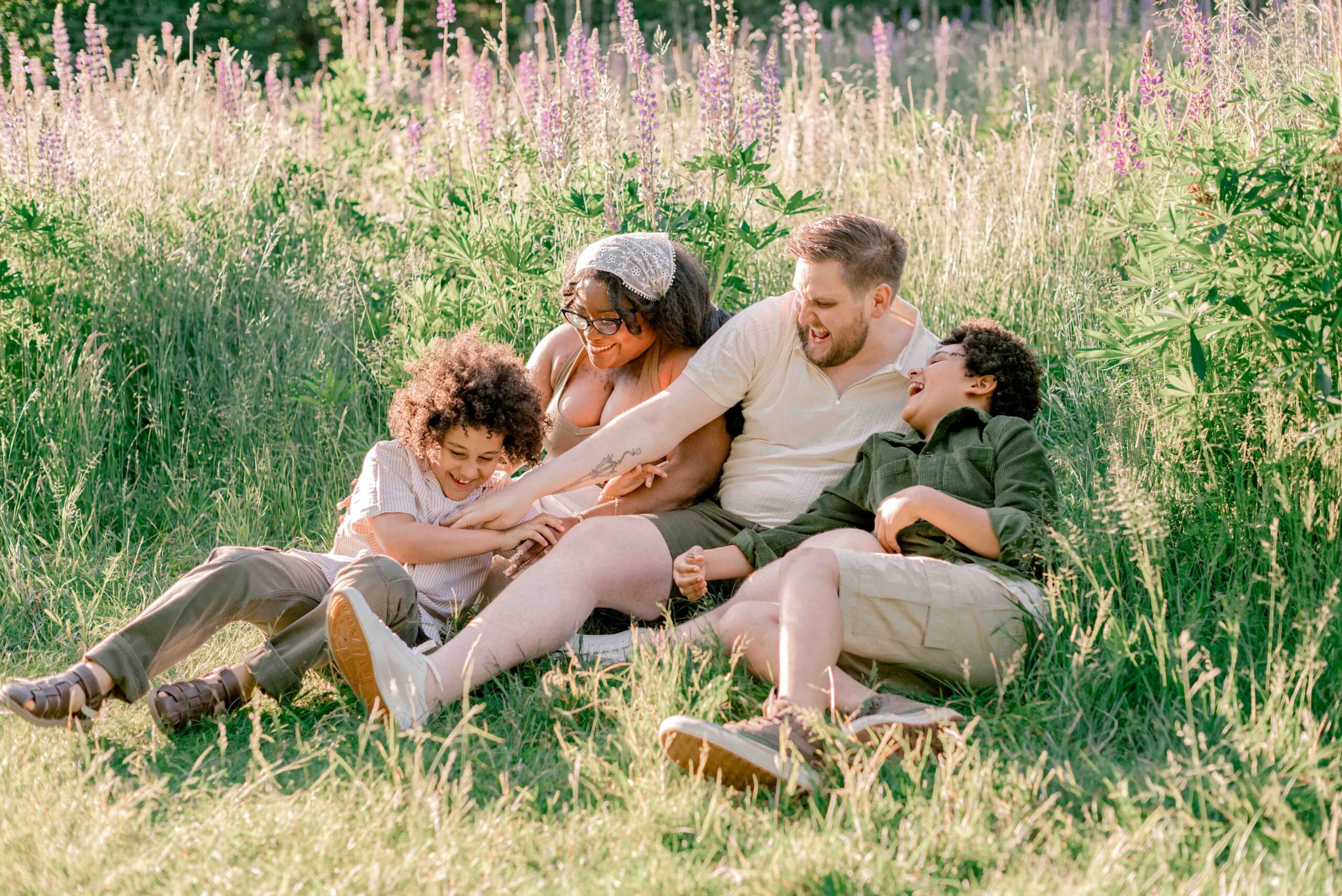 family of four sit and play in the lupine field in family photoshoot at Discovery Park